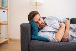 Sick Man On Couch Wondering How Long Does Food Poisoning Last