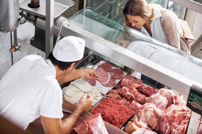 Butcher Helping Woman Purchase Raw Meat From Meat Fridge